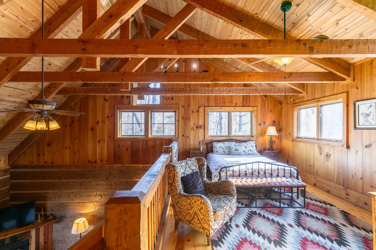 A serene bedroom scene with a plush king bed, wooden beams overhead, an inviting armchair, and windows that capture soft natural light. The space offers a tranquil setting for watching sunrises or enjoying cozy nights together, directly tying into the narrative of memorable, intimate moments.