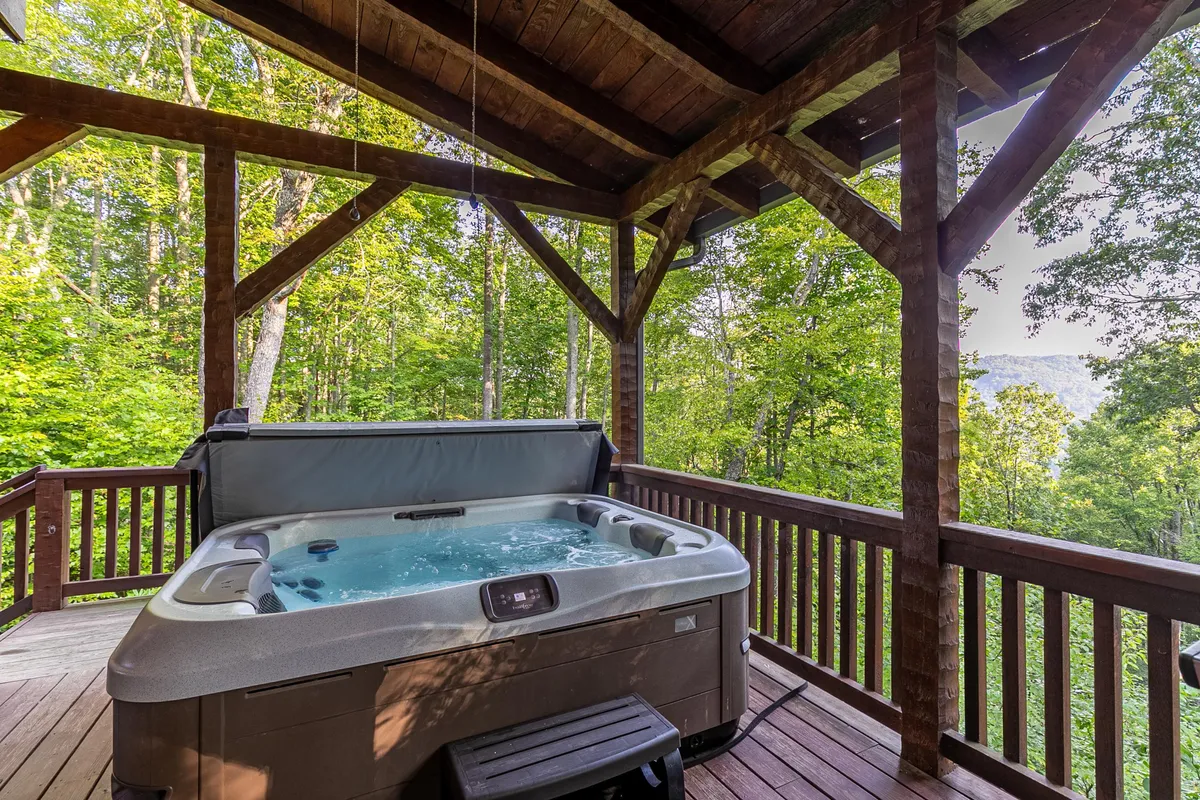 A tranquil exterior scene featuring a hot tub on the deck, embraced by tall trees. The setting offers a relaxing retreat after adventurous days, ideal for unwinding or socializing while immersed in nature.