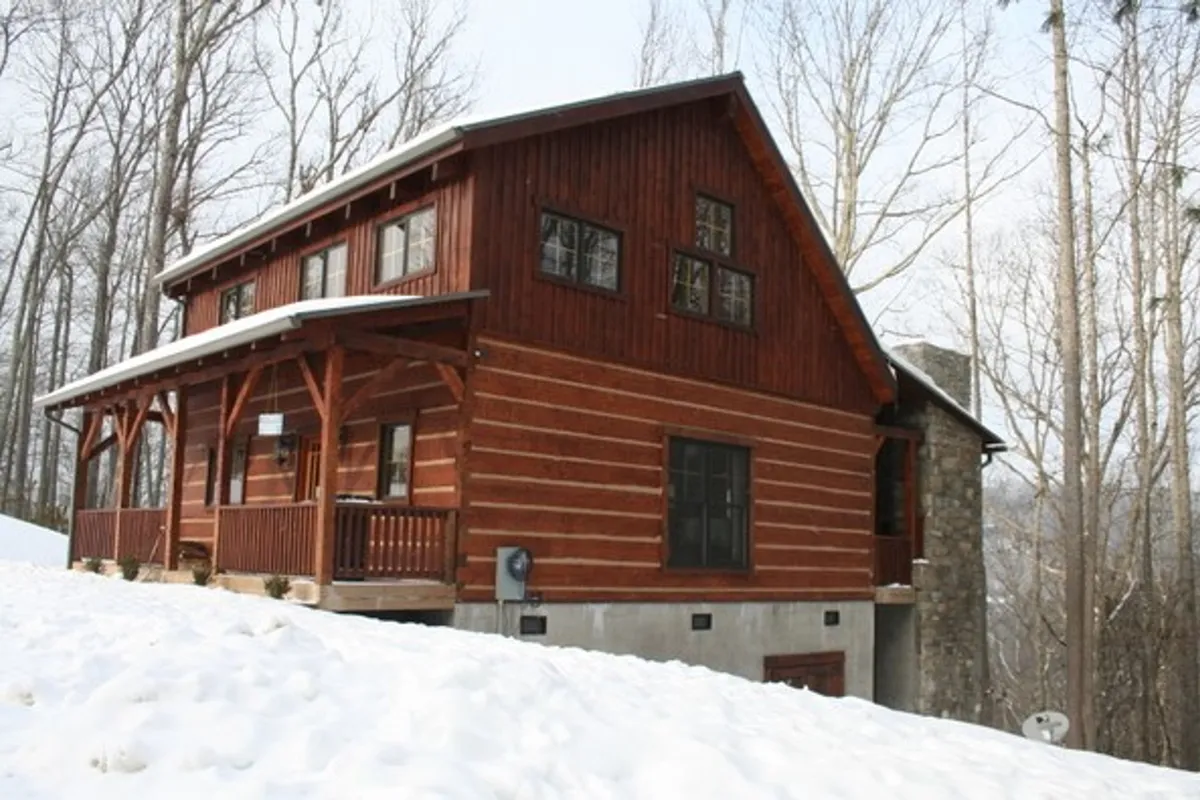 A view of the cabin's wooden structure surrounded by trees, with the ground blanketed in fresh snow. The image highlights the winter setting, demonstrating both the beauty and the adventure required for access during the colder months. The snow around the cabin sets the scene for sledding, cozy gatherings, and outdoor fun.