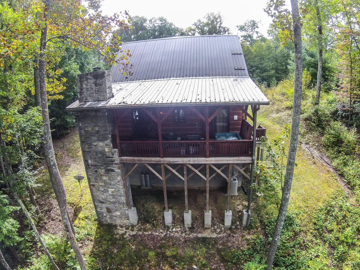 This image shows the exterior of the cabin, featuring a wooden balcony set among mature trees and a prominent stone chimney. The scene evokes a sense of peaceful seclusion with direct access to the surrounding nature, ideal for stepping outside with a pet or enjoying the fresh mountain air.