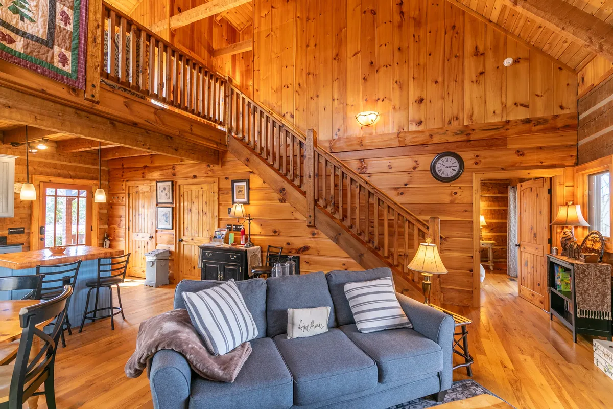 A warm, inviting living and dining area featuring a staircase, cozy sofa, decorative quilt, and a table set for family gatherings. The space is illuminated by soft lighting and decorated with natural wood accents, creating a welcoming atmosphere ideal for relaxing after outdoor adventures.