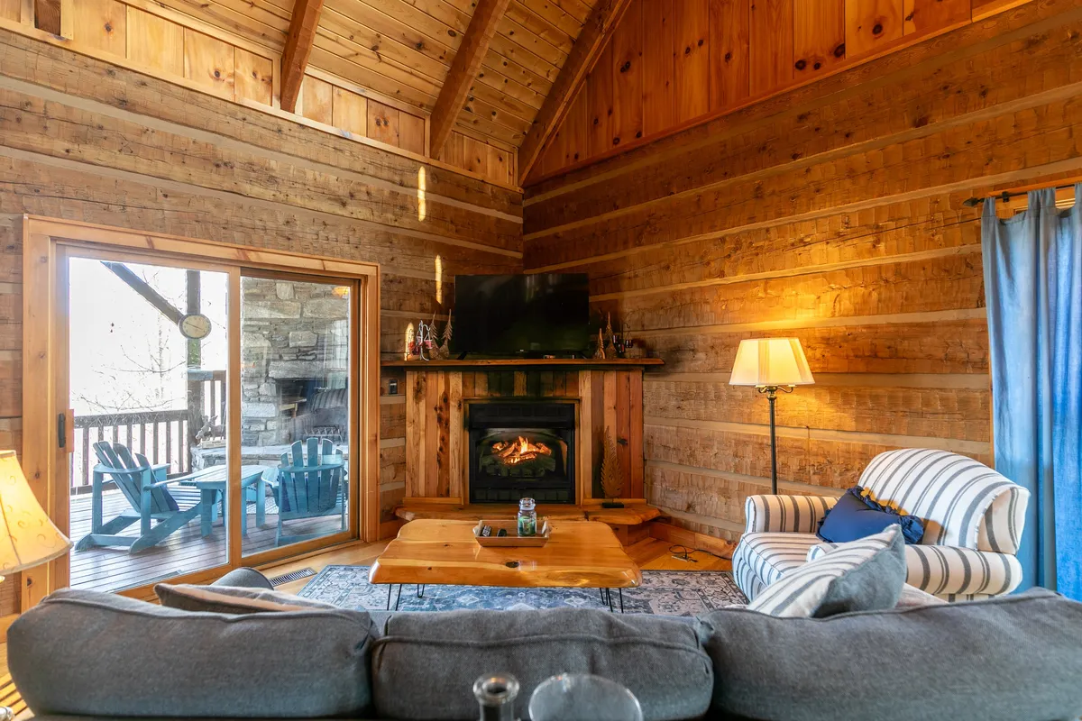 This image features a spacious living area with a cozy fireplace, wood paneling, a comfortable sofa, blue curtains, and a coffee table. The scene invites relaxation and social gatherings, ideal for movie nights or game nights with friends as described in the section.