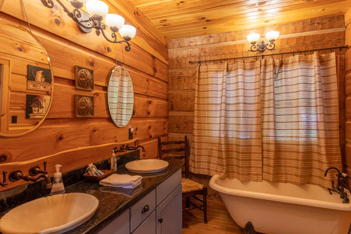 A spa-inspired bathroom featuring a freestanding clawfoot bathtub, double sinks with elegant mirrors, rustic wooden walls, and inviting light fixtures. The ambiance is peaceful and perfect for unwinding after a day outdoors.