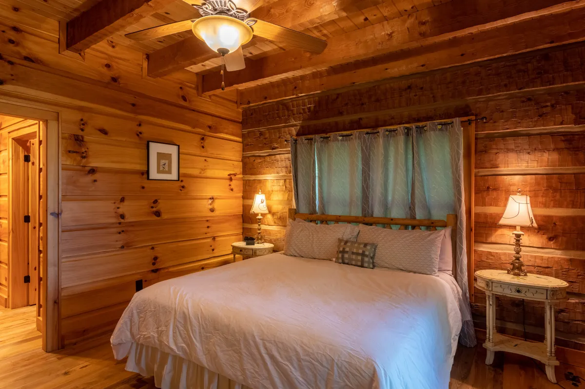 A serene bedroom with a plush bed, wooden nightstands, softly glowing lamps, and warm wooden walls. The setting exudes calm and is ideal for restful sleep, with natural light filtering softly through the window, inviting relaxation or a quiet moment with a book.