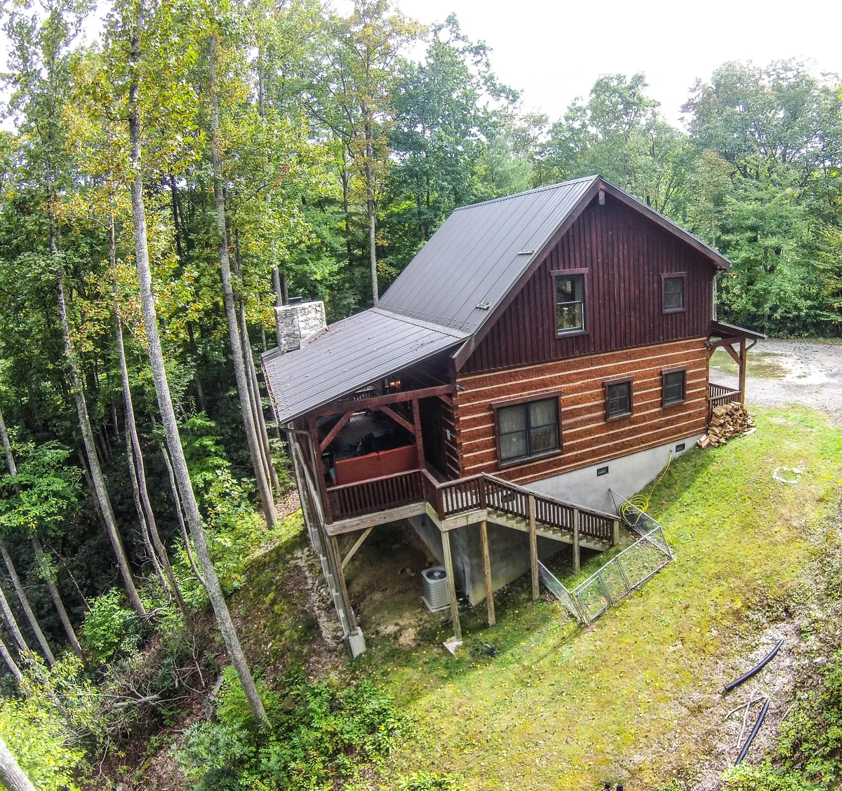 An exterior shot showing the cabin structure nestled among trees, with a spacious deck area for outdoor relaxation and gatherings. The deck suggests a perfect setting for enjoying nature in warmer months, from spring wildflower spotting to summer evenings under the stars.